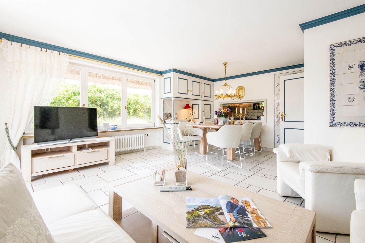 Een moderne woonkamer met een televisie, een eethoek en een keuken op de achtergrond.