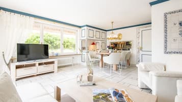 Een moderne woonkamer met een televisie, een eethoek en een keuken op de achtergrond.