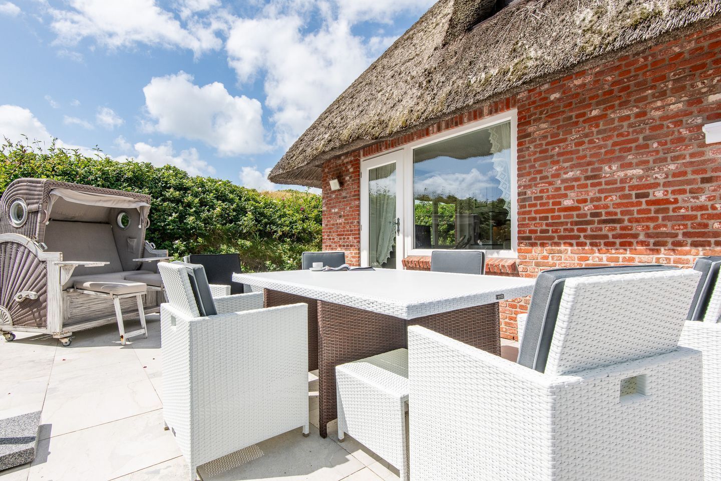 Une terrasse avec un mur en briques, un toit de chaume et du mobilier d’extérieur.