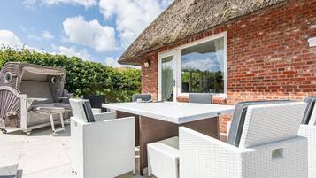 Une terrasse avec un mur en briques, un toit de chaume et du mobilier d’extérieur.