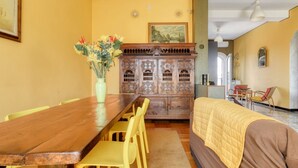 Un comedor con una mesa de madera, sillas amarillas, un aparador con adornos y un sofá con colcha.