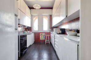 Een kleine keuken met witte kastjes, een fornuis en een raam met uitzicht.