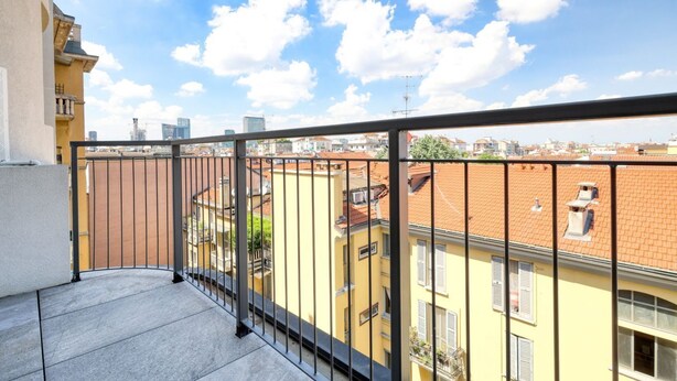 Un balcón con barandilla de metal que da a un paisaje urbano con edificios y cielo despejado.