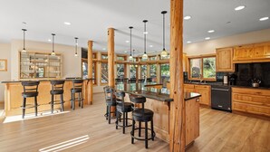 Una cocina moderna con armarios de madera, una isla central con taburetes altos, iluminación colgante y ventanas amplias.