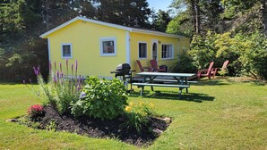 Keltainen talo, jossa on patio, ja sen ympärillä on vehreää kasvillisuutta ja puita.