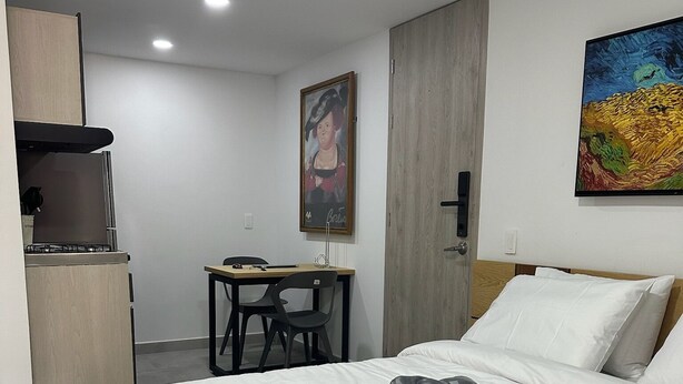 Habitación de hotel con cama, escritorio y silla. Se observa un cuadro en la pared y una puerta.