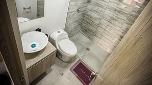 Un baño moderno con lavamanos blanco, inodoro y cabina de ducha con paredes de vidrio.