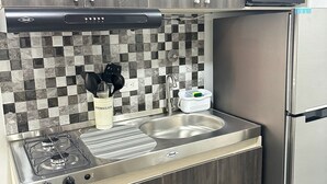 Cocina compacta con estufa a gas, pileta de acero inoxidable y microondas.