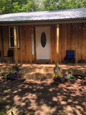 Step into this cozy cabin with a welcoming entrance, featuring a simple design and a porch with a bench and chair.