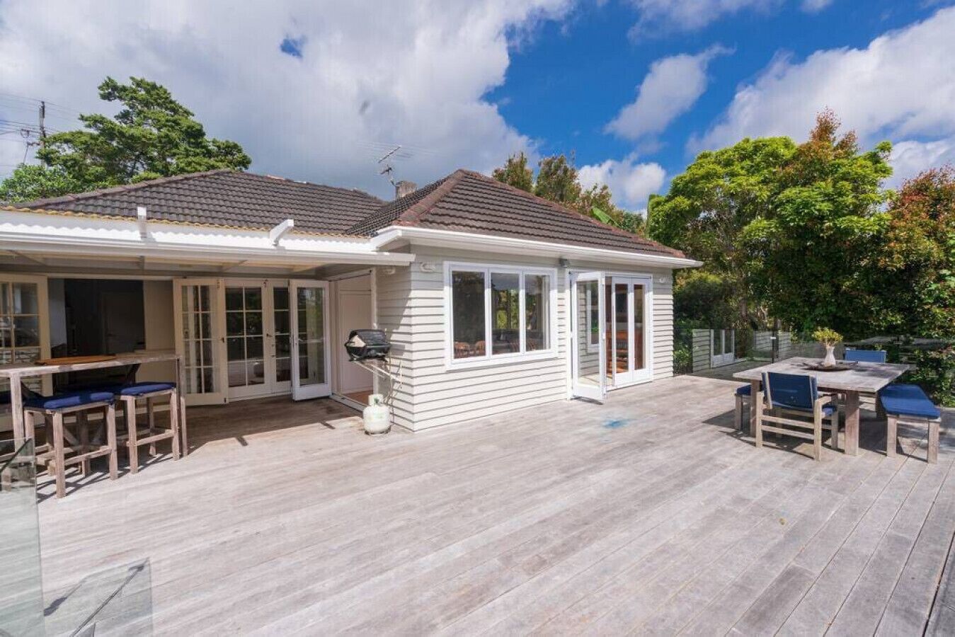 A house with a patio area, a barbecue grill, and a dining table with chairs.