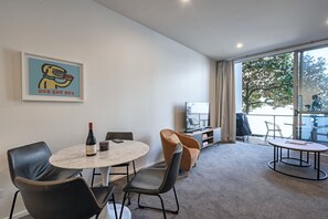 A modern hotel room with a dining area, a television, and a large window with a view of the outdoors.