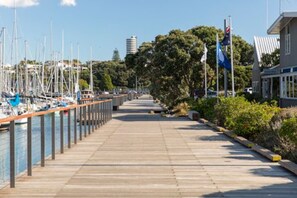 Stroll along the marina walkway, lined with boats and flags, to a dock surrounded by lush greenery and trees.