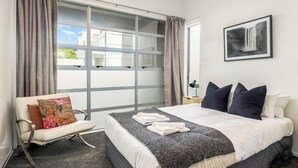 Un dormitorio con una cama grande, una silla con un cojín floral, un escritorio con una lámpara y un cuadro en la pared.