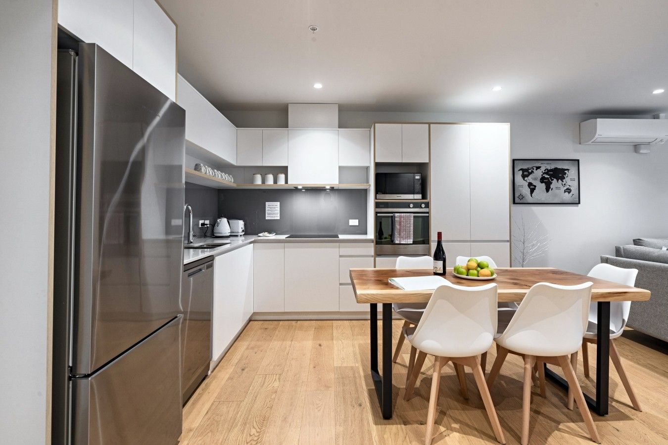 A modern kitchen with stainless steel appliances, a wooden dining table, and white chairs.