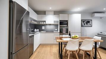A modern kitchen with stainless steel appliances, a wooden dining table, and white chairs.