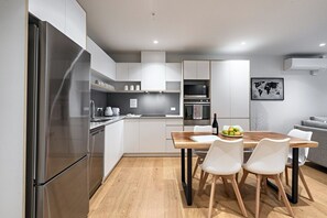 A modern kitchen with stainless steel appliances, a wooden dining table, and white chairs.
