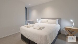 Een moderne slaapkamer met een groot bed, nachtlampjes en keurig opgevouwen handdoeken.