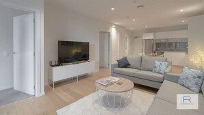 Een moderne woonkamer met een flatscreen televisie, een grijze bank en een salontafel.