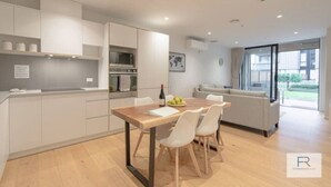 Een moderne keuken met witte kasten, een houten eettafel en een bank in de aangrenzende woonkamer.