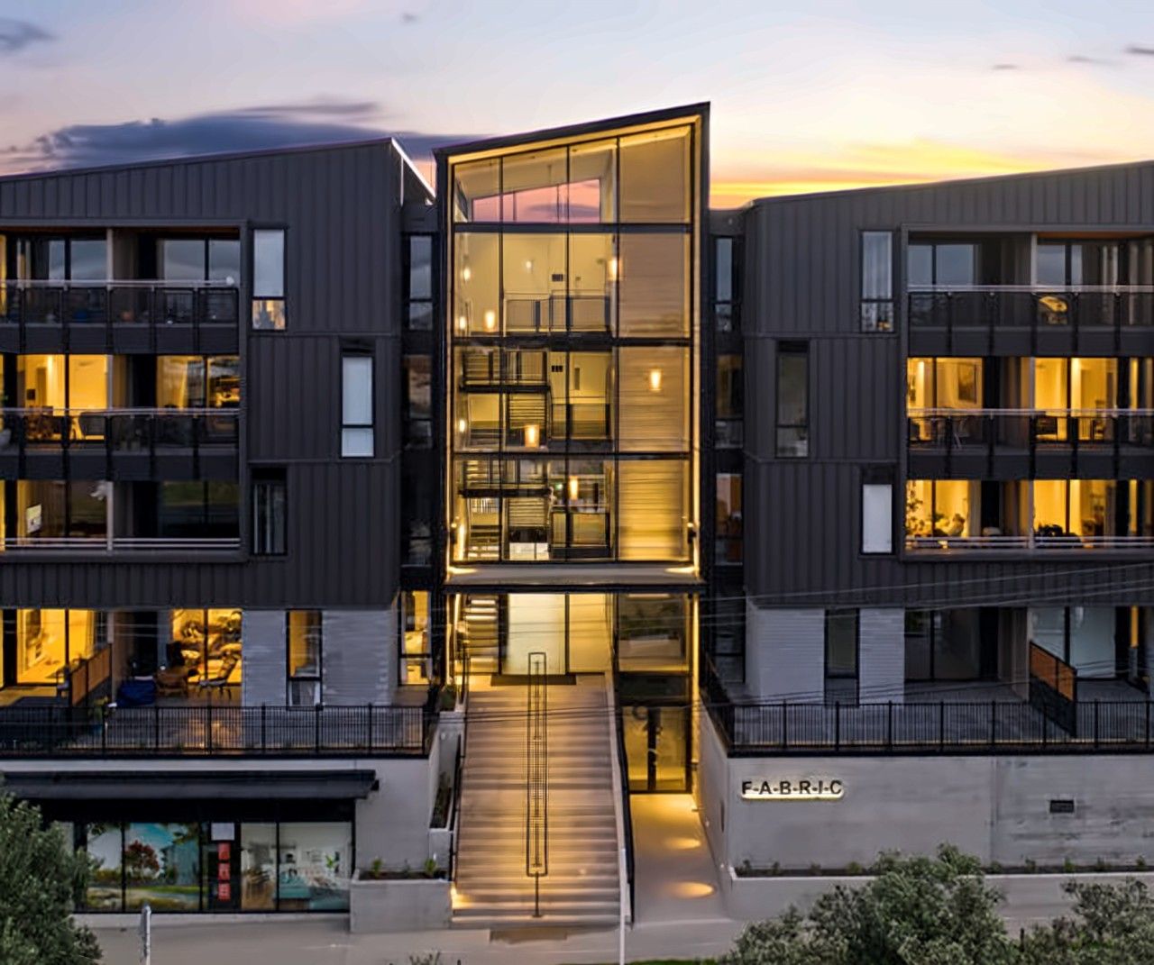 Un immeuble moderne à plusieurs étages, doté d’une façade en verre, de nombreux balcons et d’une entrée bien visible.