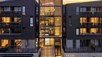 A modern multi-story building with a glass facade, multiple balconies, and a visible entrance.