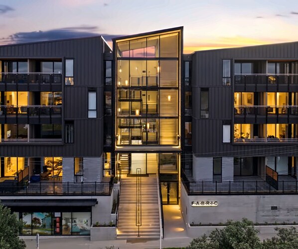 A modern multi-story building with a glass facade, multiple balconies, and a visible entrance.