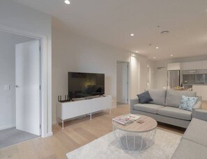Un salon moderne avec un téléviseur à écran plat, un canapé gris et une table basse.