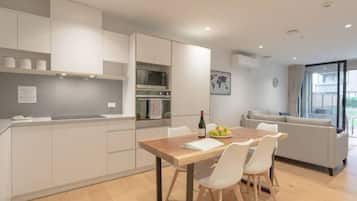A modern kitchen with white cabinets, a wooden dining table, and a sofa in the adjacent living area.