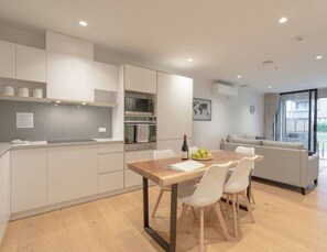 Une cuisine moderne avec des meubles blancs, une table à manger en bois et un canapé dans le salon attenant.