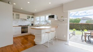 A modern kitchen with white cabinetry, a wooden island with stools, and a view of the backyard through large windows.