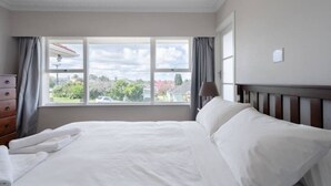 A hotel room with a large window, a bed, a dresser, and a lamp.