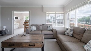 A modern living room with a sofa, a coffee table, and a view of a garden through large windows.