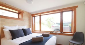 A bedroom with a bed, pillows, a chair, and a window with a view of a car outside.