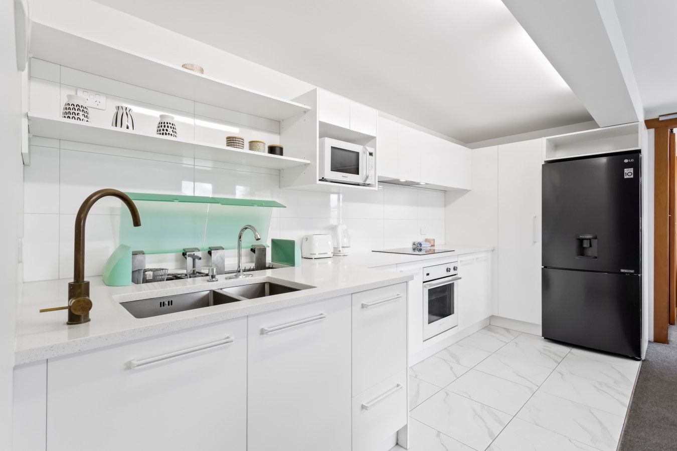 A modern kitchen with white cabinetry, a stainless steel sink, a black refrigerator, and a microwave.