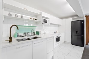 A modern kitchen with white cabinetry, a stainless steel sink, a black refrigerator, and a microwave.