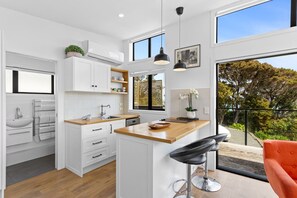 A modern kitchen with white cabinetry, a wooden countertop, and a bar stool. - Cosy Tiny Home with Ocean Views|by Furnished Rentals (Auckland)