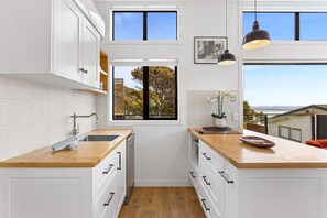 A modern kitchen with white cabinetry, wooden countertops, a window with a view, and pendant lighting. - Cosy Tiny Home with Ocean Views|by Furnished Rentals (Auckland)