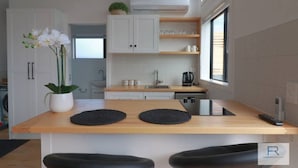 A modern kitchen with white cabinets, a wooden countertop, and a black pendant light. - Cosy Tiny Home with Ocean Views|by Furnished Rentals (Auckland)