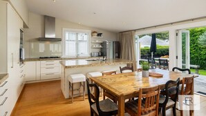 Une cuisine moderne dotée d’un îlot central, de meubles blancs et d’un coin repas avec une table et des chaises en bois.