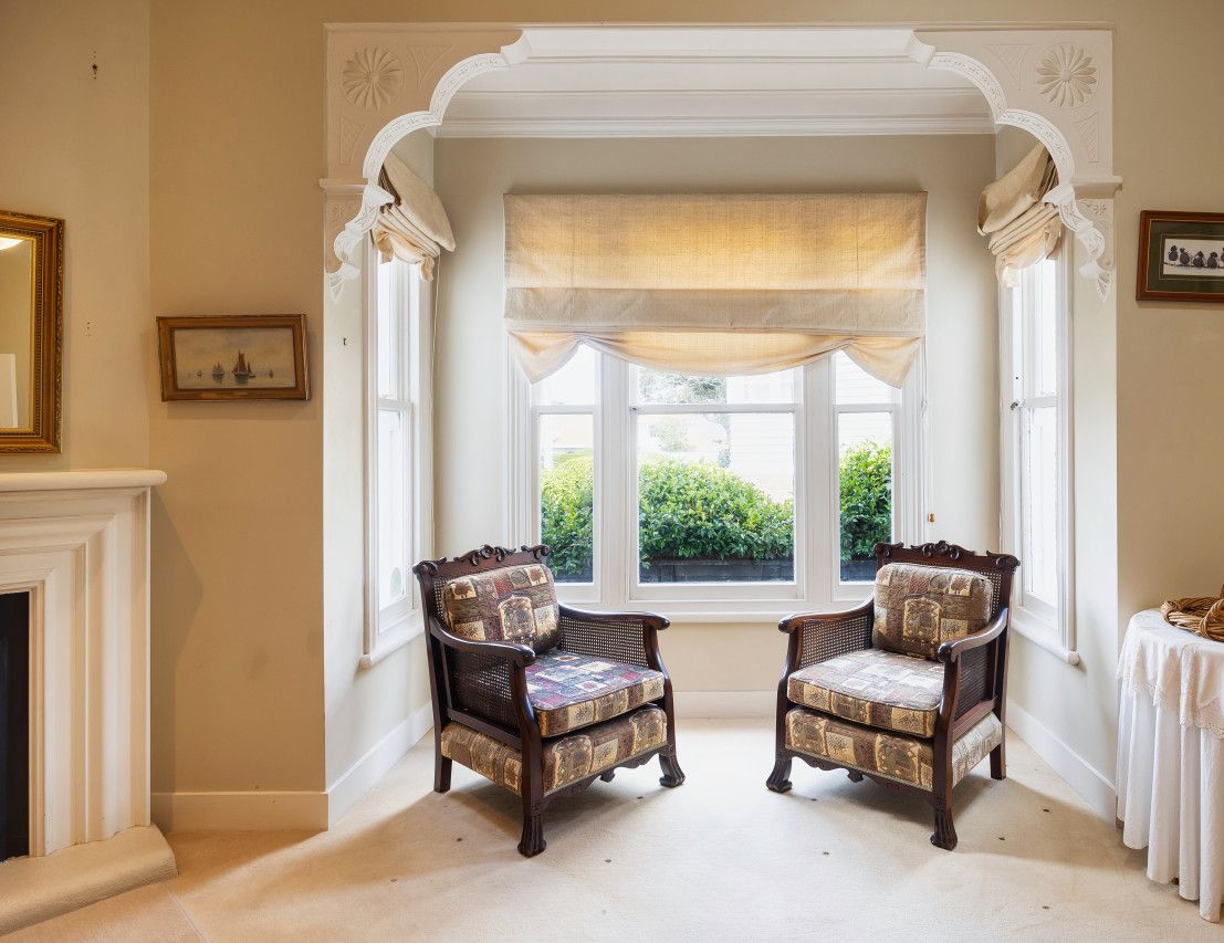 A room with two upholstered chairs, a fireplace, a window with a valance, and a small table with a basket.