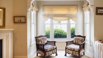 A room with two upholstered chairs, a fireplace, a window with a valance, and a small table with a basket.