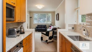 A compact kitchen with a microwave, toaster, and sink. There is a seating area with a black and white chair and a sofa. - Spacious Mt Eden Apartment|by Furnished Rentals (Auckland)