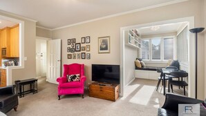 A living room with a pink armchair, a TV on a wooden stand, a dining area with a table and chairs, and a bookshelf. - Spacious Mt Eden Apartment|by Furnished Rentals (Auckland)