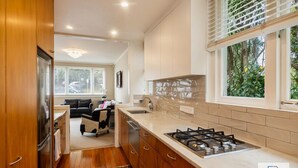 A modern kitchen with wooden cabinets, a gas stove, and a large window with blinds. - Spacious Mt Eden Apartment|by Furnished Rentals (Auckland)