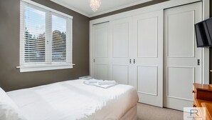 A bedroom with a large bed, white curtains, a chandelier, and a TV on the wall. - Spacious Mt Eden Apartment|by Furnished Rentals (Auckland)