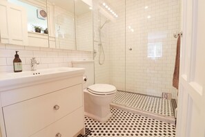 Une salle de bain avec des carreaux blancs, des toilettes, un lavabo et une douche.