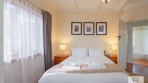 A neatly made bed with white linens, two bedside lamps, and a framed picture above the bed.