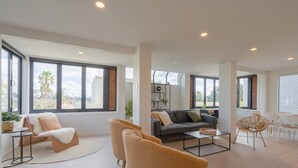 A spacious living area with large windows, a sofa set, a coffee table, and a dining area.