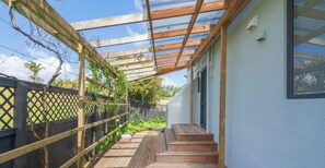 Un espacio al aire libre techado con escalones de madera que conducen a la entrada de un edificio, una pérgola de madera y una valla de celosía.