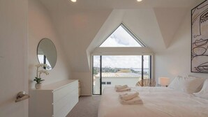 A bedroom with a large bed, a dresser, a mirror, and a view of the city through a skylight.